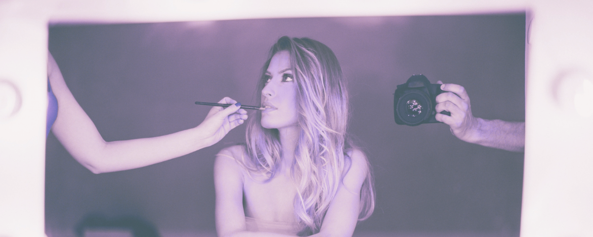 headshot of woman in mirror getting makeup touch up with camera on right